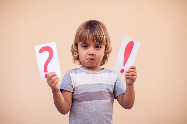 Photo portrait d'enfant garçon tenant des cartes avec point d'exclamation et point d'interrogation. les enfants et le concept de l'éducation