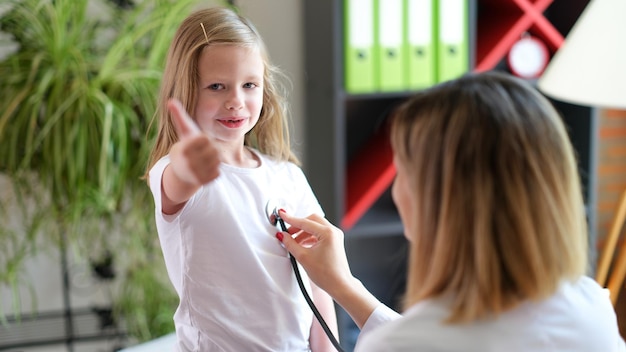 Portrait d'un enfant joyeux et joyeux au rendez-vous chez le médecin pédiatre montrant le geste du pouce vers le haut