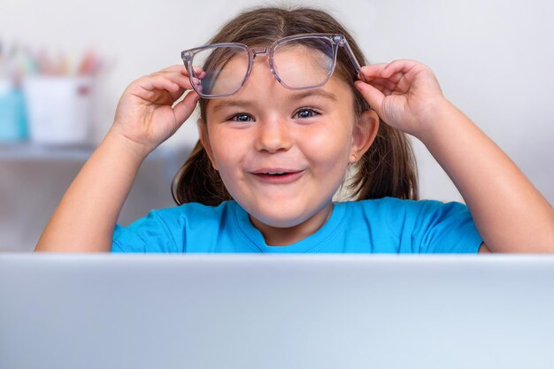 Portrait de l'enfant à lunettes jetant un coup d'œil surpris derrière un ordinateur portable