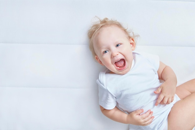 Portrait d'enfant mignon. Amusant bébé qui rit heureux sur un matelas blanc dans une chambre blanche. Textile et literie pour enfants. Enfant regardant dans la caméra. Famille heureuse. Fermer.