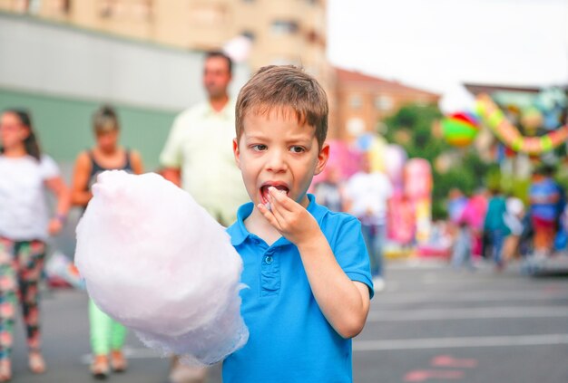 Portrait d'enfant mignon mangeant de la barbe à papa sur un fond de festival d'été