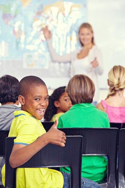 Photo portrait d'un enfant noir et pouce levé d'un élève en classe à l'école primaire ou en classe éducation drôle et enfant avec un geste de la main pour un accord emoji ou un signe de succès et d'approbation