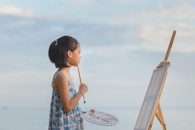 Portrait d'une enfant peignant sur la toile à la plage Une enfant heureuse dessinant un tableau en plein air