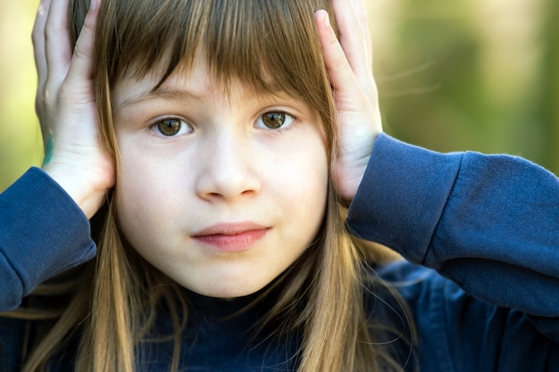 Portrait d'enfant surpris fille tenant par la main à sa tête à l'extérieur en été. Enfant femelle choquée par une chaude journée à l'extérieur.