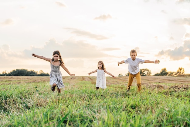 Portrait d'enfants jouant au jeu de capture et de saut en cours d'exécution sur des chemins de champs de foin d'herbe sèche au lever du soleil