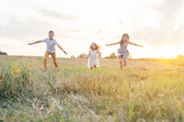 Portrait d'enfants jouant au jeu de capture et de saut en cours d'exécution sur des chemins de champs de foin d'herbe sèche au lever du soleil