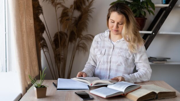 Portrait d'un enseignant caucasien assis à une table avec des livres à la maison près de la fenêtre Une femme se prépare pour une conférence L'éducation à la maison