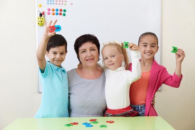 Portrait d'un enseignant préscolaire mature et d'enfants dans une salle de classe pendant les cours