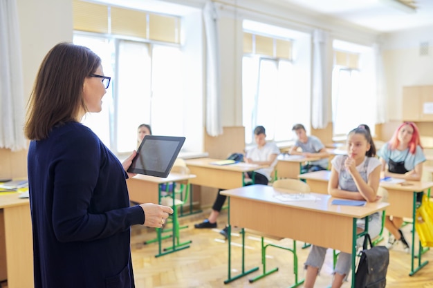Portrait d'une enseignante d'âge moyen qui parle dans une salle de classe avec des élèves adolescents