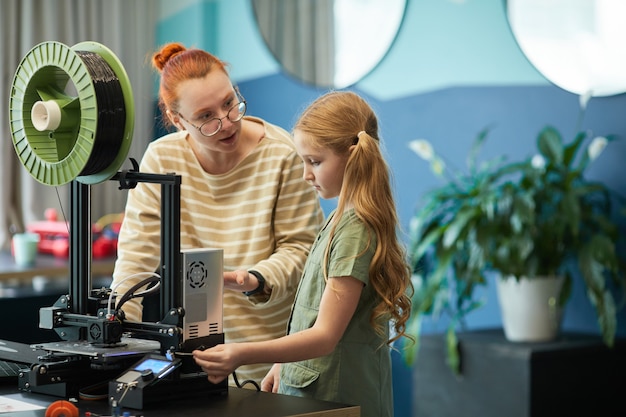 Portrait D'une Enseignante Aidant Une Jolie Fille à L'aide D'une Imprimante 3d Pendant Le Cours D'ingénierie Et De Robotique à L'école Moderne, Espace De Copie