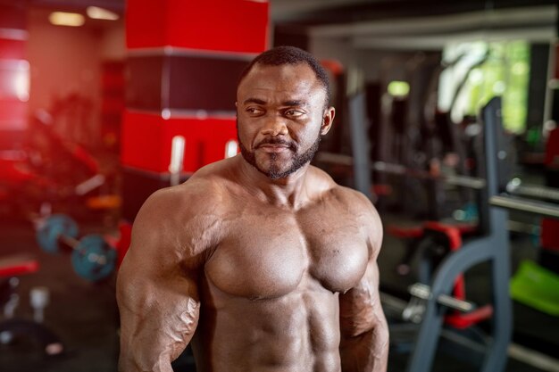 Portrait d'un entraîneur de fitness masculin afro-américain Bodybuilder montrant ses biceps et regardant sur le côté de l'arrière-plan de la salle de sport