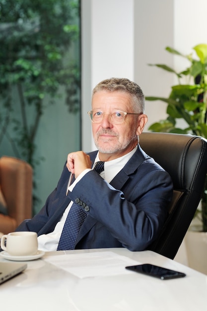 Photo portrait d'entrepreneur d'âge moyen assis au bureau avec contrat et tasse de café en face de lui