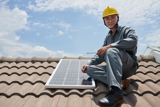 Portrait d'un entrepreneur asiatique souriant installant des panneaux solaires sur le toit de la maison