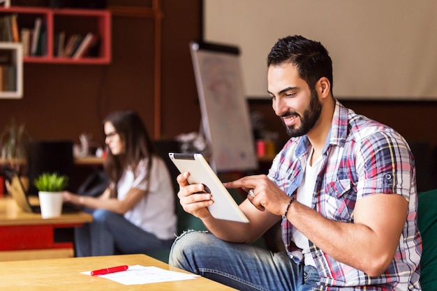 Portrait d'un entrepreneur barbu utilisant un ordinateur tablette pour les affaires assis près d'une table dans un bureau moderne