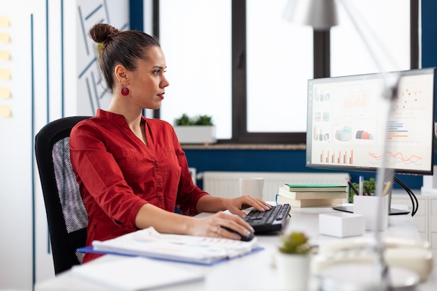 Portrait d'un entrepreneur concentré travaillant et analysant des graphiques financiers, sur des écrans d'ordinateur assis sur un bureau en train de taper. Cadre de démarrage faisant des recherches en regardant des graphiques.