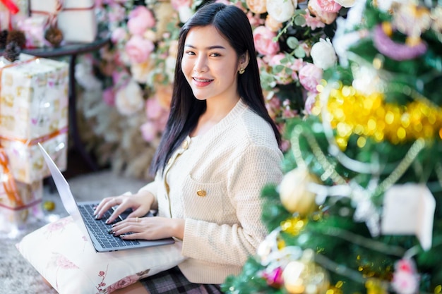 Portrait d'entreprise indépendante beau sourire positif jeune femme asiatique en ligne travaillant avec un ordinateur portable à la maison dans le salon à l'intérieur Décoration Pendant les vacances de Noël et du Nouvel An.