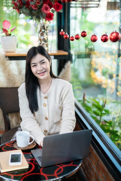 Portrait d'entreprise indépendante beau sourire positif jeune femme asiatique en ligne travaillant avec un ordinateur portable et un smartphone sur un ordinateur portable à la maison dans le salon à l'intérieur ou au caféBusiness Lifestyle