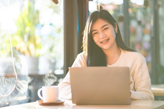 Portrait entreprise indépendante beau sourire positif jeune femme asiatique en ligne travaillant avec un ordinateur portable et une tasse de café à la maison dans le salon à l'intérieur ou au caféBusiness Lifestyle