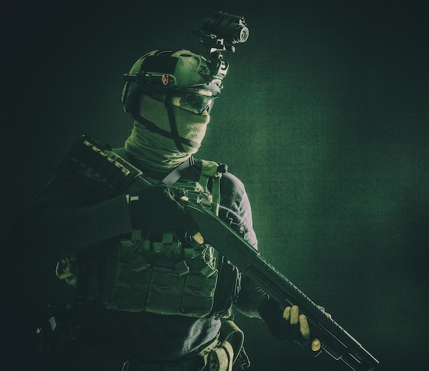 Portrait d'épaule des troupes d'élite de l'armée soldat équipe tactique antiterroriste avec casque de fusil de chasse avec imageur thermique cachant le visage derrière un fusil armé de masque avec tir de studio à portée optique sur noir