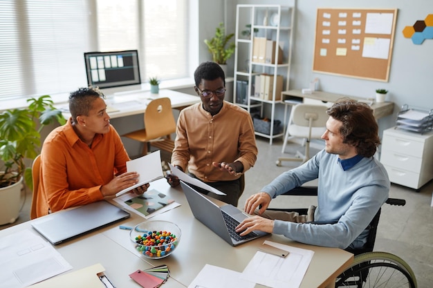 Portrait d'une équipe commerciale diversifiée discutant d'un projet à la table de réunion se concentrant sur un jeune homme utilisant une roue