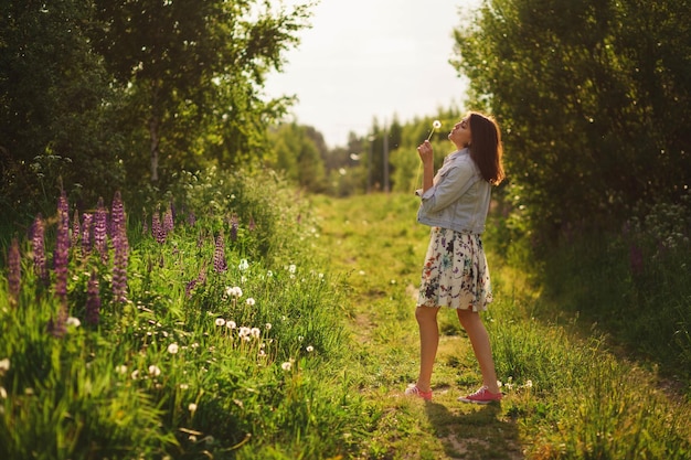 Portrait d'été atmosphérique d'une belle fille brune dans une veste en jean tenant une fleur