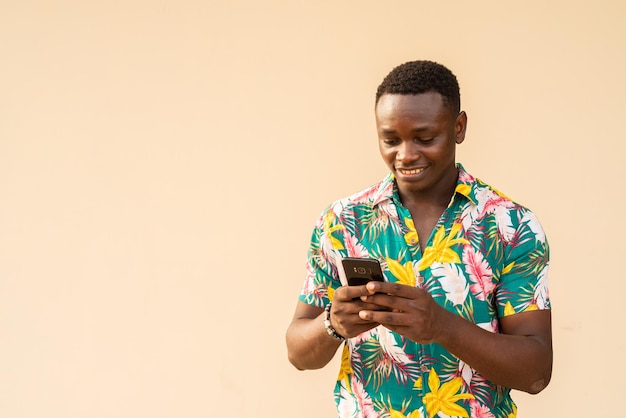 Portrait d'été d'un bel homme africain profitant de vacances et utilisant un téléphone portable