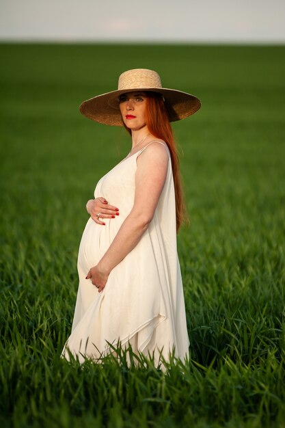 Portrait d'été de belle femme enceinte marchant sur le champ vert