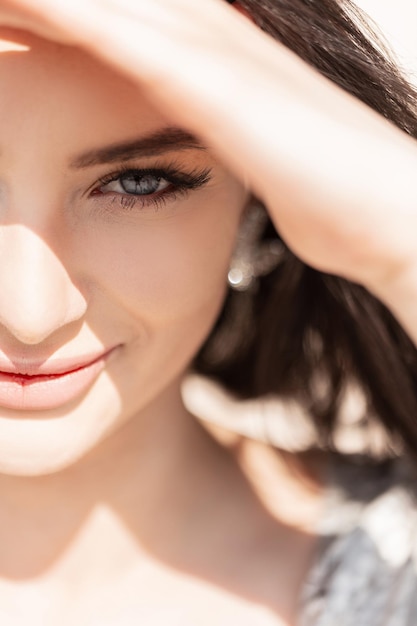 Portrait d'été frais féminin d'une belle fille heureuse aux yeux bleus demi-visage La belle femme couvre ses yeux de la lumière du soleil et regarde dans l'appareil photo Beauté et été