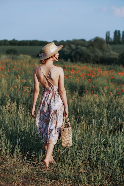 Portrait d'été en plein air d'une adolescente avec des fraises panier, chapeau de paille. Une fille sur une route de campagne, vue arrière. Fond de nature, paysage rural, pré vert, style campagnard