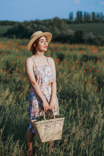 Portrait d'été en plein air d'une adolescente avec des fraises panier, chapeau de paille. Une fille sur une route de campagne, vue arrière. Fond de nature, paysage rural, pré vert, style campagnard