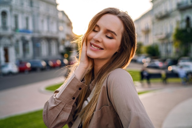 Portrait d'été en plein air d'une femme blonde élégante et heureuse s'amusant dans la rue, ambiance de voyage dans le temps au coucher du soleil