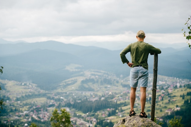 Portrait d'été de style de vie par derrière de l'homme avec un bâton en bois debout au sommet de la montagne avec un beau paysage à l'avant. Voyageur masculin appréciant la vue sur la nature depuis le plus haut sommet de la colline.