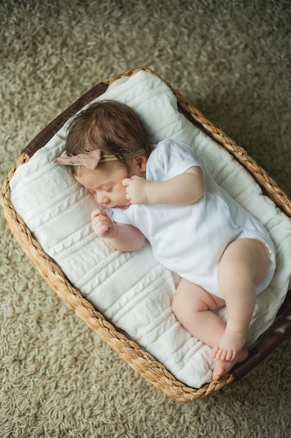 Portrait étroit d'un bébé mignon de 2 mois fille dans des vêtements blancs dans un panier en osier