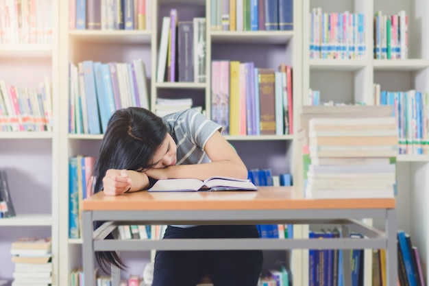 Portrait d&#39;étudiant asiatique intelligent épuisé pour lire et faire des recherches dans la bibliothèque du collège