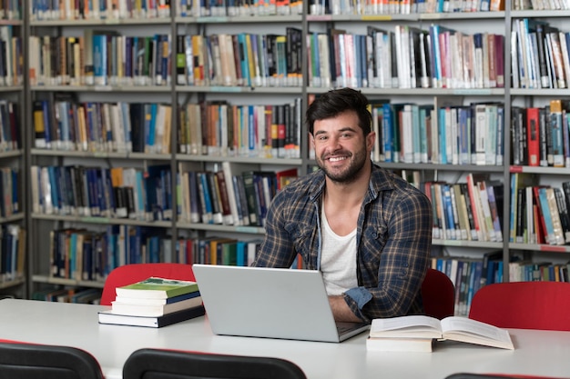 Portrait d'un étudiant attrayant faisant du travail scolaire avec un ordinateur portable dans la bibliothèque