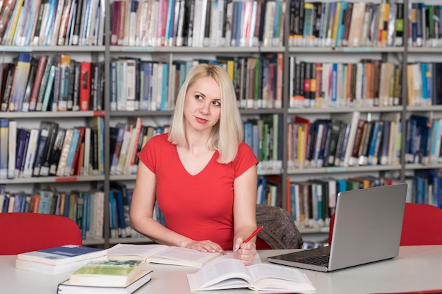 Portrait d'un étudiant attrayant faisant du travail scolaire avec un ordinateur portable dans la bibliothèque