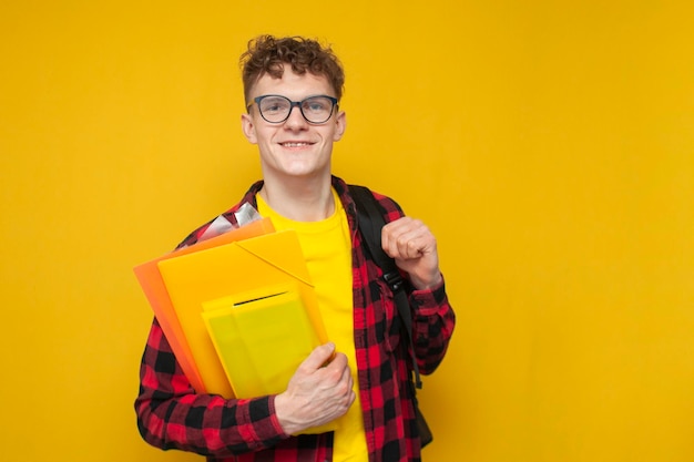 Portrait d'un étudiant dans des verres avec un sac à dos et des livres sur fond jaune