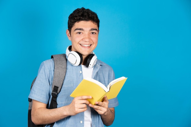 Portrait d'étudiant hispanique tenant un livre isolé sur fond bleu