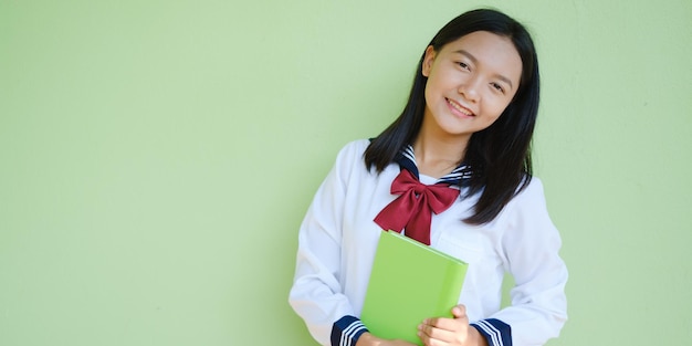 Portrait étudiant jeune fille à l'école uniforme avec livre vert sur fond vert, fille asiatique, adolescente.