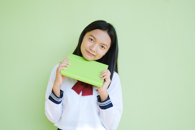 Portrait étudiant jeune fille à l'école uniforme avec livre vert sur mur vert. Adolescent fille asiatique