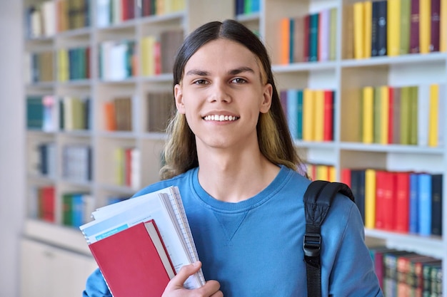 Portrait d'un étudiant avec des livres, des manuels, regardant la caméra dans la bibliothèque du collège.