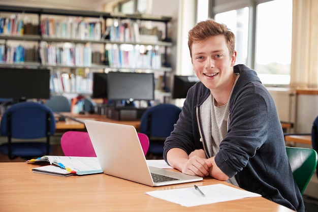 Portrait d'un étudiant travaillant sur un ordinateur portable dans la bibliothèque du collège