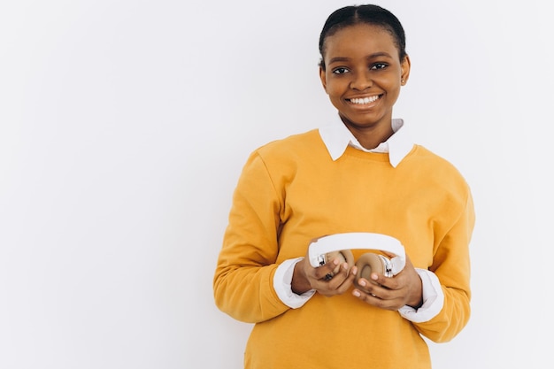 Portrait d'une étudiante afro-américaine heureuse dans une veste jaune tenant des écouteurs blancs et dansant