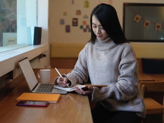Portrait d'étudiante à faire ses devoirs avec de la papeterie et un ordinateur portable sur le comptoir bar dans un café