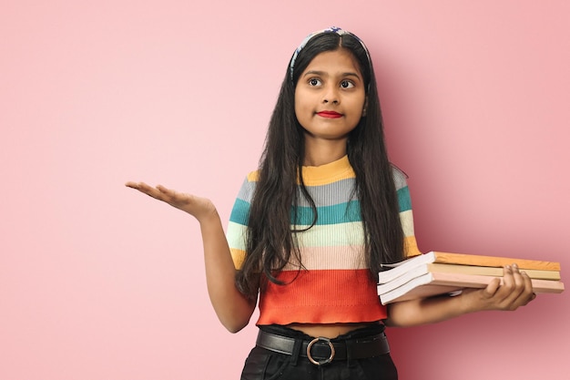 Portrait d'une étudiante indienne asiatique confuse et désemparée posant isolé tenant un espace de copie sur la paume et des livres d'autre part regardant vers le haut comme ne sachant pas quoi faire ensuite