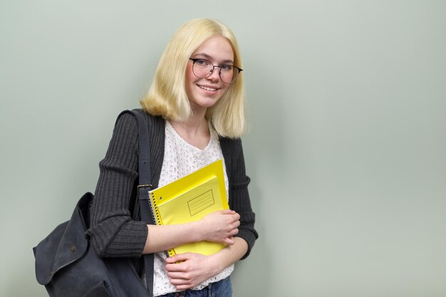 Portrait d'une étudiante souriante heureuse adolescente de 16 ans dans des verres avec des manuels de sac à dos regardant la caméra, sur fond de couleur verte, espace pour copie