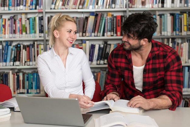 Portrait d'étudiants attrayants faisant du travail scolaire avec un ordinateur portable dans la bibliothèque