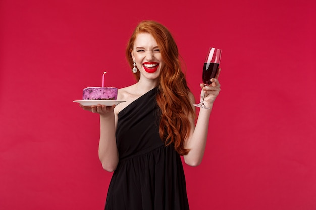 Portrait, de, excité, rire, magnifique, roux, femme, amusant, à, b-day, partie, tenant verre verre vin, et, gâteau anniversaire, à, bougie allumée, faire voeu, célébrer, sur, mur rouge