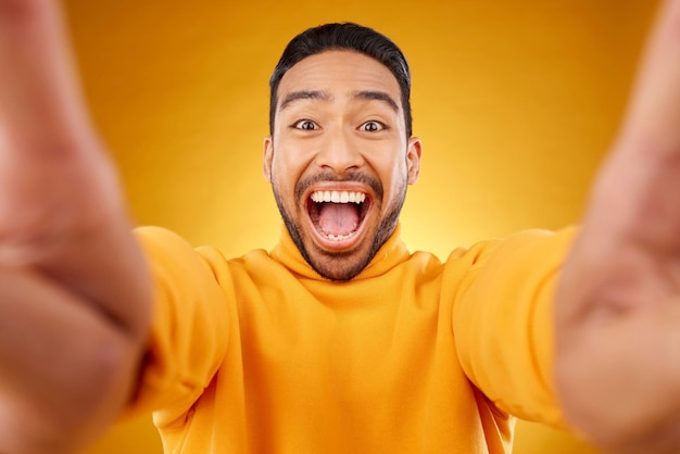 Portrait excité et selfie d'un homme heureux en studio isolé sur fond jaune Sourire du visage et personne asiatique prenant une photo de profil pour un souvenir amusant en riant et en photographie sur les réseaux sociaux