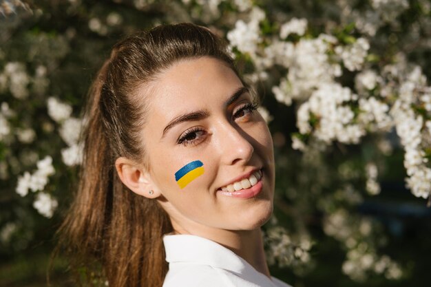 Portrait extérieur d'une femme ukrainienne avec un drapeau ukrainien bleu et jaune sur sa joue sur la cerise